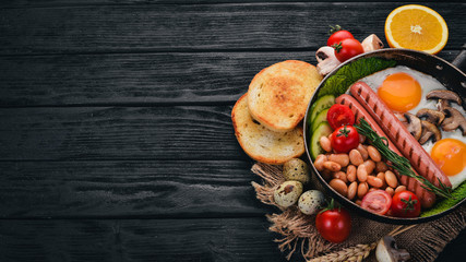 Full English breakfast with fried eggs, sausages, beans, toasts and coffee on copy space background. On a black wooden background.