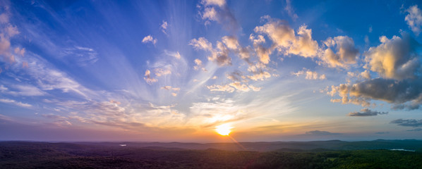Panoramic sunset with light, puffy clouds in the sky overlooking summer New England forests. High resolution HDR panorama from drone