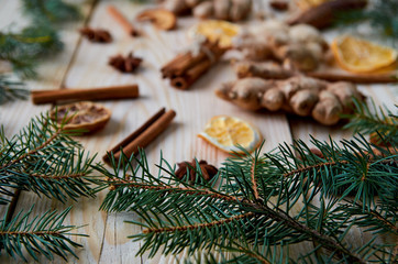 Christmas tree branches close up on the foreground. Traditional spices for mulled wine, Christmas bakery: cinnamon, anise stars, ginger, dried oranges, apples on the blurred wooden background