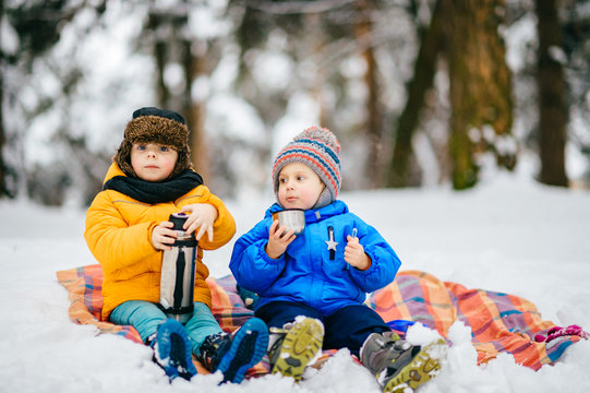 Funny Children Winter Party In Snowy Forest. Kids Male Friends Rest Outdoor At Nature. Young Boys Sharing And Drinking Tea From Thermos. Hot Drinks And Beverage In Cold Weather. Warming In Frost Day.