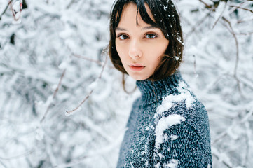 Closeup sensual soft focus portrait of young teenager girl. Emotional amazing beautiful big dark eyes of brunette female looking at camera outdoor in snowy winner forest. Tender, innocent child face.