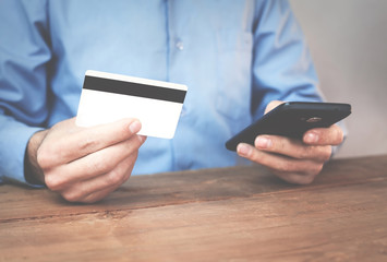 Man holding credit card and using phone.