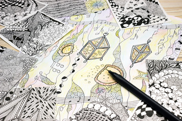 An overhead photo of the abstract doodle patterns made of black liner pen on the wooden table. Pen strokes. Doodle, tangle illustration. Zen art, sketch illustration. Lesson for artist, painters.