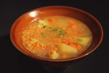 Dish with tasty lentil soup on black background