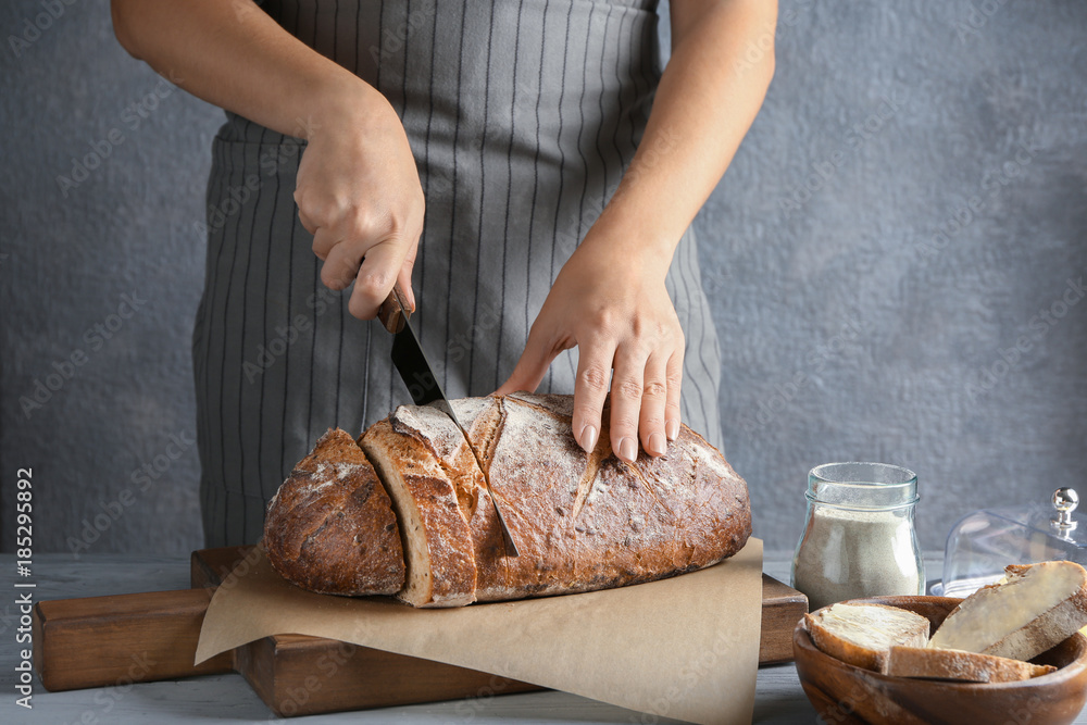 Wall mural Woman cutting buckwheat bread on wooden board in kitchen