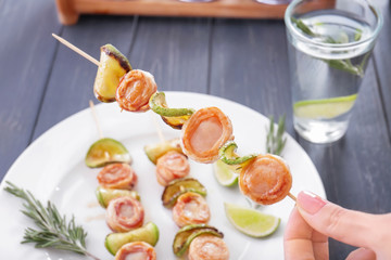 Woman holding bamboo skewer with bacon wrapped scallops, closeup