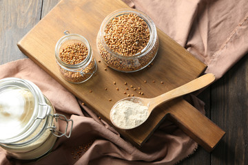 Buckwheat flour and raw grains in kitchenware on wooden board