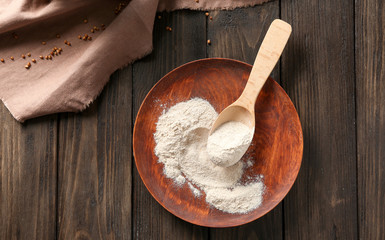 Wooden plate and spoon with buckwheat flour on table