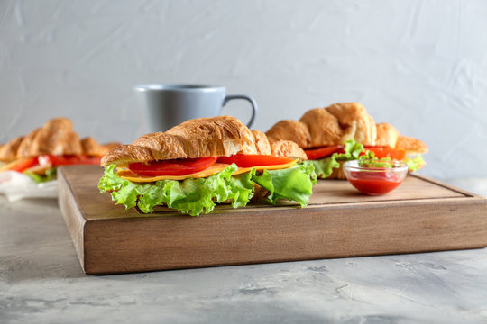 Wooden board with delicious croissant sandwiches on table