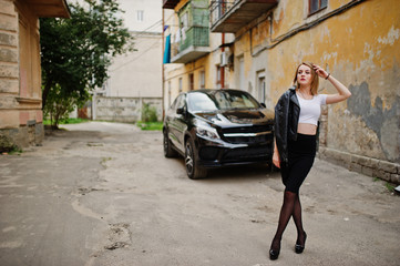 Elegant blonde girl wear on black leather jacket posing at streets of town background luxury car.