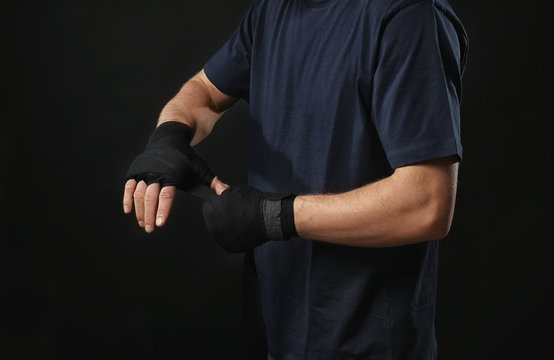 Male boxer applying wrist wraps on black background, closeup