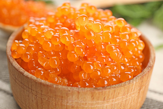 Wooden bowl with delicious red caviar on table, closeup