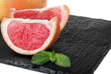 Whole grapefruit and two slices with leaf of mint on the slate p