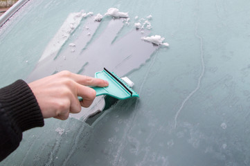 Man is cleaning frozen front car window with ice scraper.