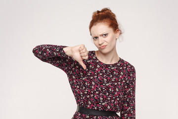 Ginger woman showing thumb down isolated on a gray background.