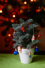 a little decorated Christmas tree in pot on the table with lights on big christmas tree in background