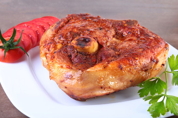 grilled pork chop with sliced tomato and sauce on wooden table.
