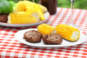 Plate with delicious grilled patties and corn cobs on table