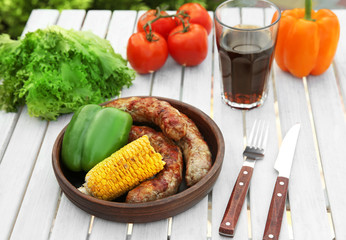 Plate with delicious grilled sausages and vegetables on wooden table outdoors