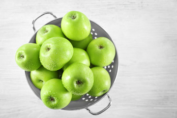 Colander with fresh green apples on wooden background