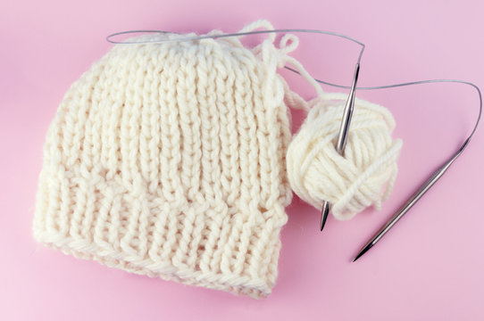 Vintage Knitting needles and yarn on a pink background, a cap tied with white natural wool. With the blur. DYV