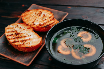 Vegetable soup decorated with sliced carrots and green parsley and crunchy wheat toasts on dark wooden table. Appetizing first courses menu, kitchen background, restaurant concept