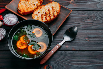Vegetable soup decorated with sliced carrots and green parsley and toasts, flat lay with copy space on dark wooden table. Appetizing first courses menu, kitchen background, restaurant concept