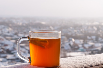 Transparent cup with hot spicy drink, lemon and orange on the background of the winter city