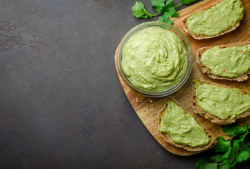 Traditional mexican homemade guacamole sauce in a glass bowl and sliced bread on a dark black stone background. Top view, copy space, horizontal
