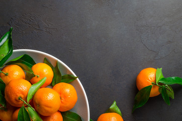 Fresh clementines on a gray plate on a dark black stone backgrou