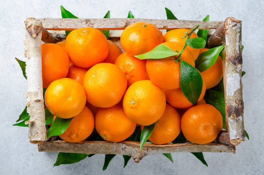 Fresh clementines in a wooden box on a light stone background. T