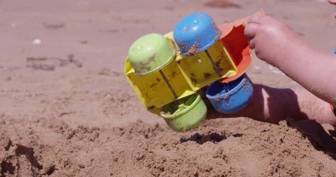 Toddler playing with toy dumptruck on beach - extreme close up