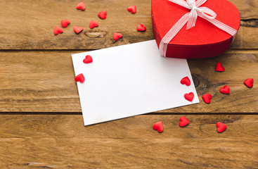 Blank valentines greeting card and small red gift box on wooden table