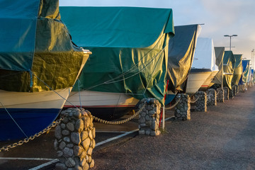Boats covered with tarpaulin in winter storage - obrazy, fototapety, plakaty