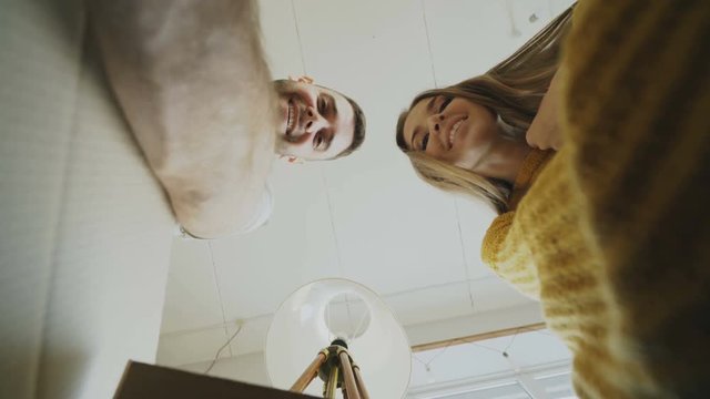 POV of happy couple kissing while opening cardboard box after relocation and looking inside and taking things in new house