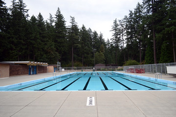 Outdoor swimming pool surrounded by tall evergreen trees. Water sport in the middle of a forest in Vancouver, British Columbia, Canada