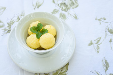 Butter balls with garnish in a bowl with saucer on a fabric tablecloth
