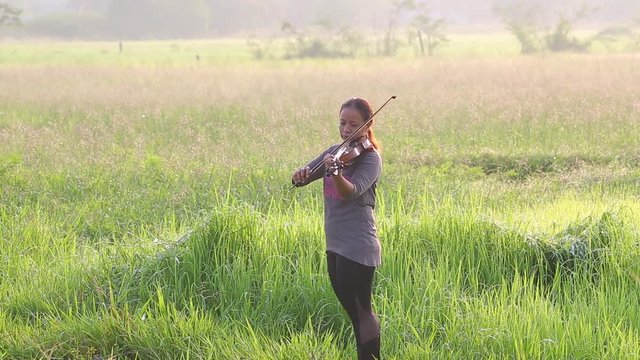 an asian woman playing violin on grass field in the morning