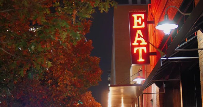 A nighttime view of a red neon "EAT" sign on the side of a restaurant in a large city.  	