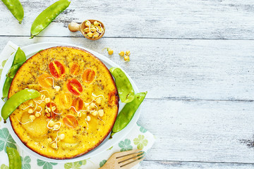Close-up of frittata (omelet) with potato, tomato and young pea on a white table with copy space. Rustic lunch concept.