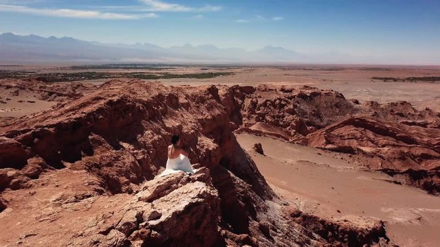 Aerial view of model wearing bride dress contemplating the rocky desert, 4k