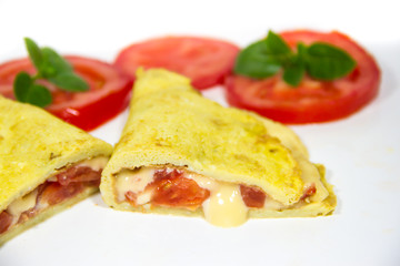 omelette made with beaten eggs stuffed with onion cheese and tomatoes on white background with sliced tomatoes and basil