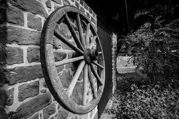 Fototapeta na wymiar A wooden wheel from a cart hangs on a brick wall. Black and white.