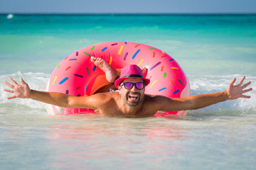 Happy handsome smiling man in pink hat swims on big inflatable tube at the coast of Caribbean Sea in summer sunny day