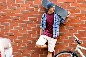 Teenage boy with skateboard standing next to the wall