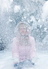 Beautiful blonde young woman has fun and throws snow up in winter forest