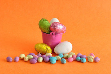 A bucket filled with easter eggs and some small ones laying next to it
