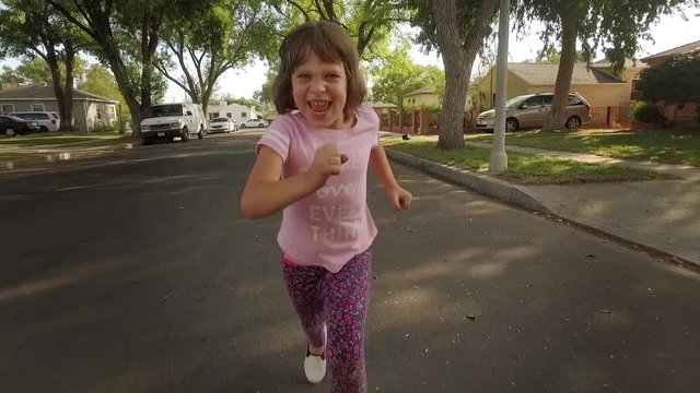 Happy 5 Year Old Girl Running On Suburban Street, Chasing POV Camera Slow Motion