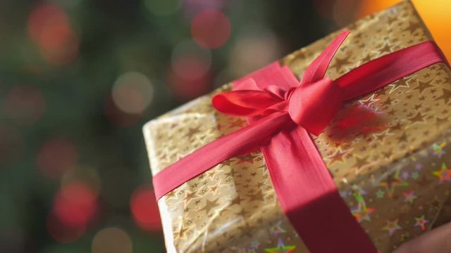Close up gift, a large gift box wrapped in golden paper with a red ribbon on a bright festive background