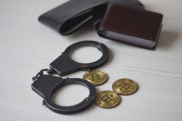 Golden bitcoins, handcuffs and the purse on the wooden table